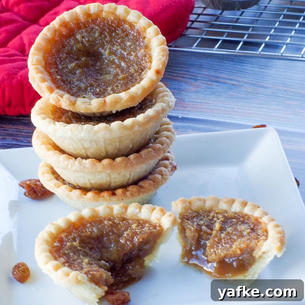 21 Patriotic Canada Day Desserts 20 4 butter tarts stacked on a white plate, with a butter tart split in half in front of the stack