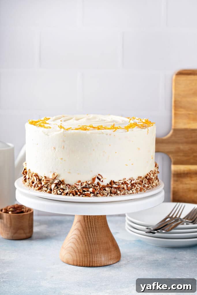 Carrot Cake Recipe with Grand Marnier Cream Cheese Frosting 13 Cream cheese frosted carrot cake decorated with chopped pecans and orange zest on a cake stand.