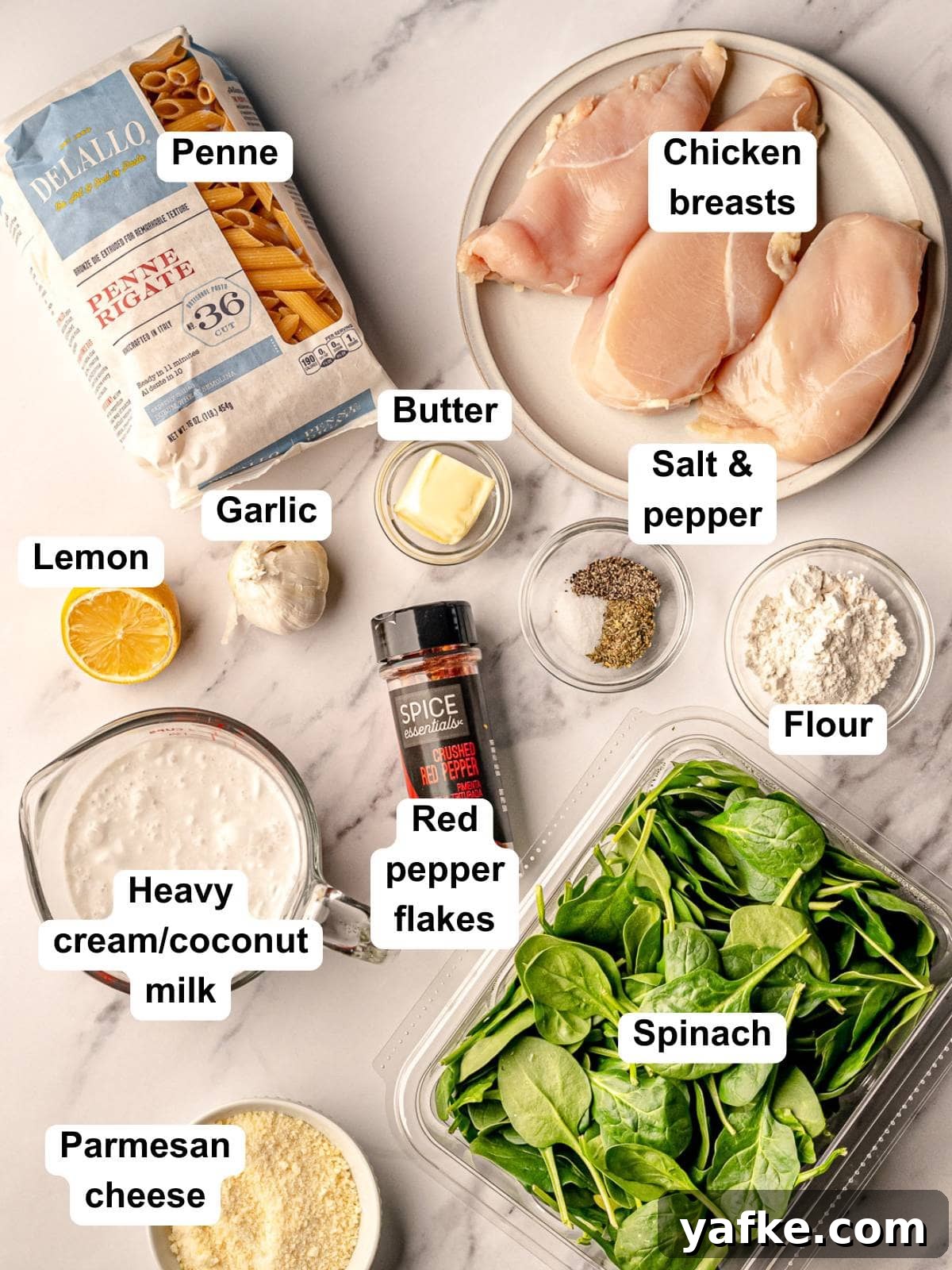 30-Minute Garlic Parmesan Chicken Pasta Recipe 3 Flat lay of ingredients for creamy garlic parmesan chicken pasta, including penne pasta, raw chicken breasts, fresh spinach, garlic, butter, flour, salt, pepper, red pepper flakes, lemon, grated parmesan cheese, and a measuring cup of heavy cream or coconut milk.