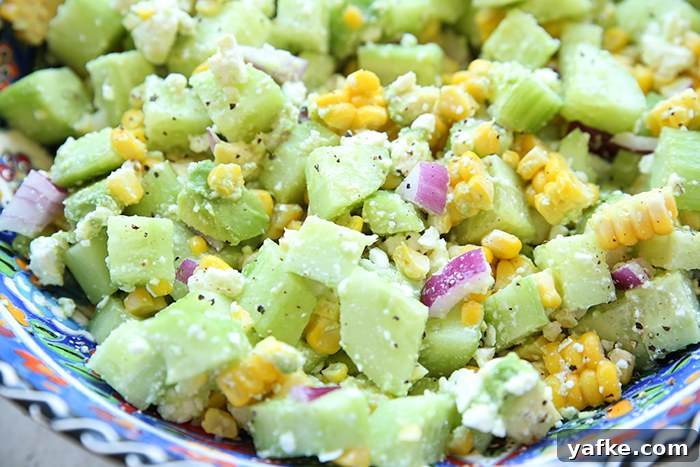 A partial picture of a serving bowl filled with summer cucumber salad with feta and red onion.