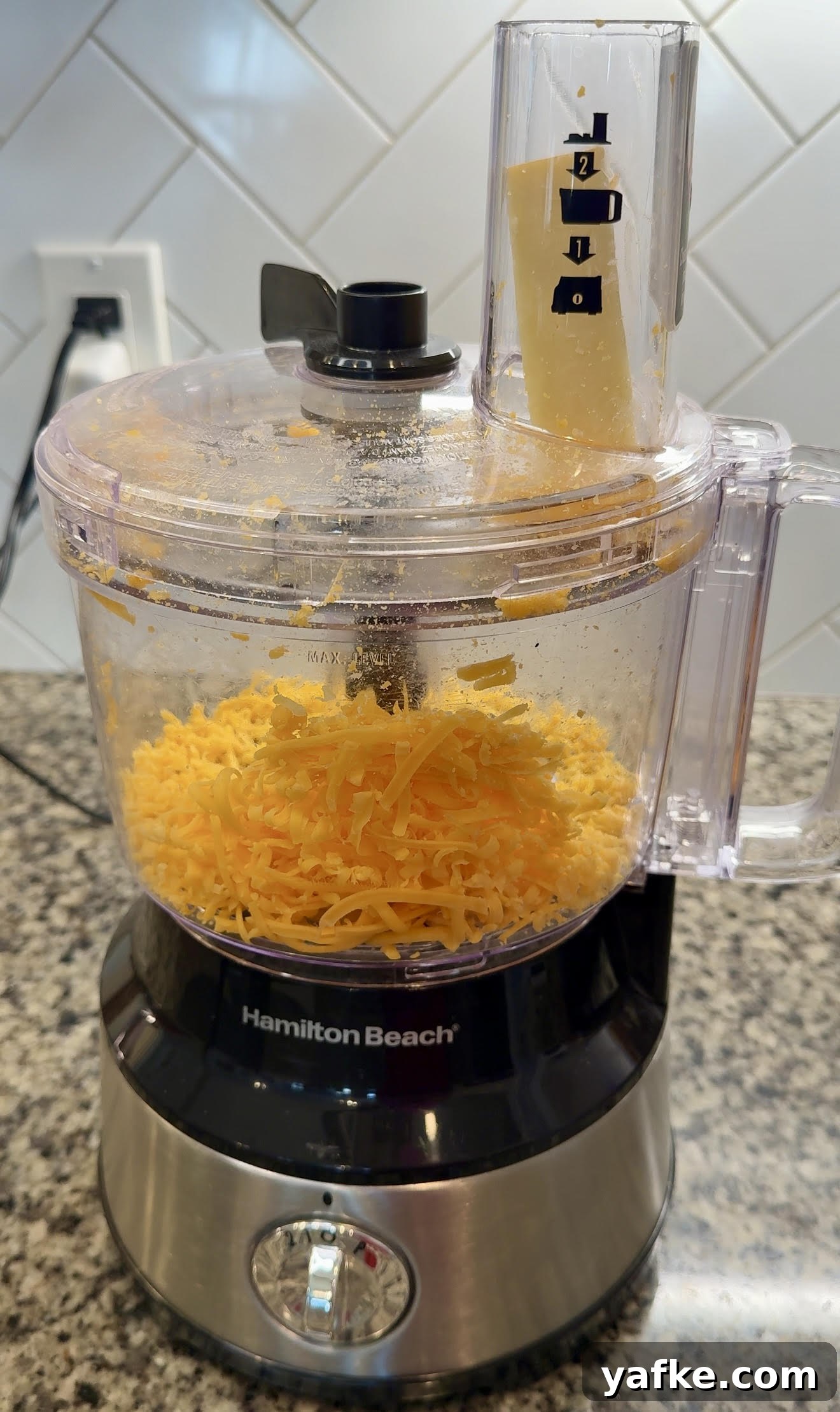 Southern Soul Food Baked Mac and Cheese Recipe 5 Food processor with a block of cheddar cheese in the chute, ready to be shredded.
