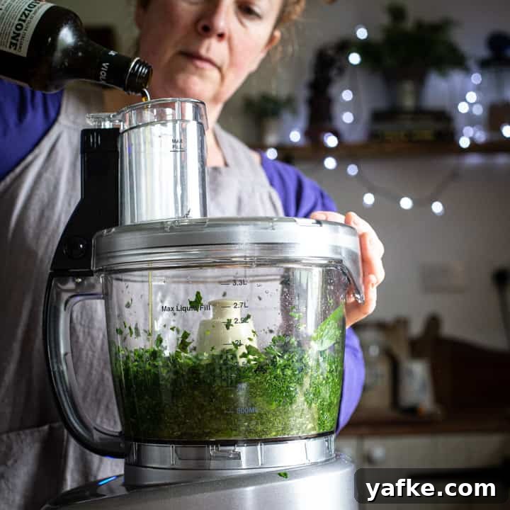 Wild Garlic Pesto Recipe for Spring 6 woman in grey pouring olive oil into a food processor to make fresh pesto