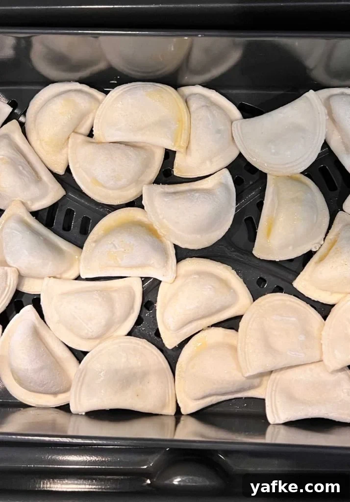 Crispy Air Fryer Pierogies in 15 Minutes 4 mini frozen pierogies in air fryer tray with olive oil spray