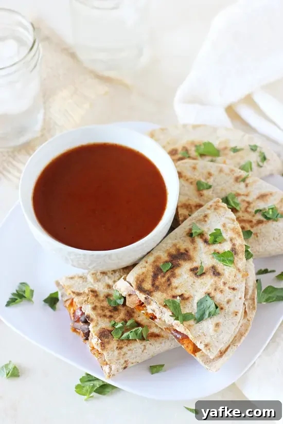 Plenty of veggies, spices, black beans and of course cheese make these roasted vegetable quesadillas a weeknight staple! A simple vegetarian recipe that can double as an appetizer! Roasted Vegetable Quesadillas on a white plate with a bowl of enchilada sauce.