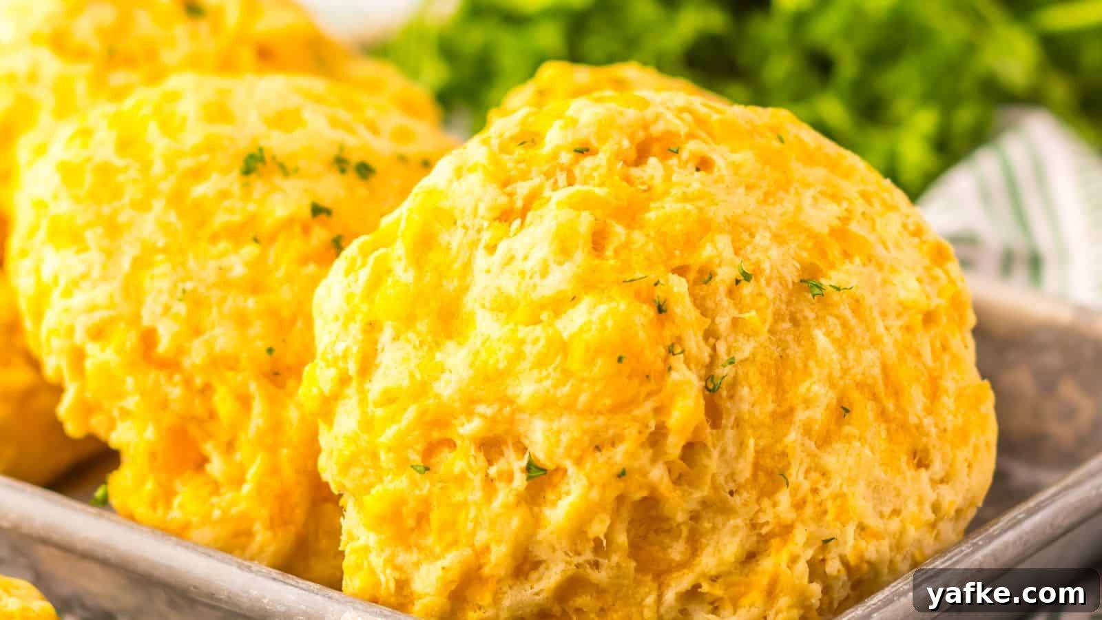 21 Fall Snacks I Tried: 9 Keepers 19 Close-up of fluffy cheddar biscuits topped with herbs on a metal tray, with leafy greens in the background.