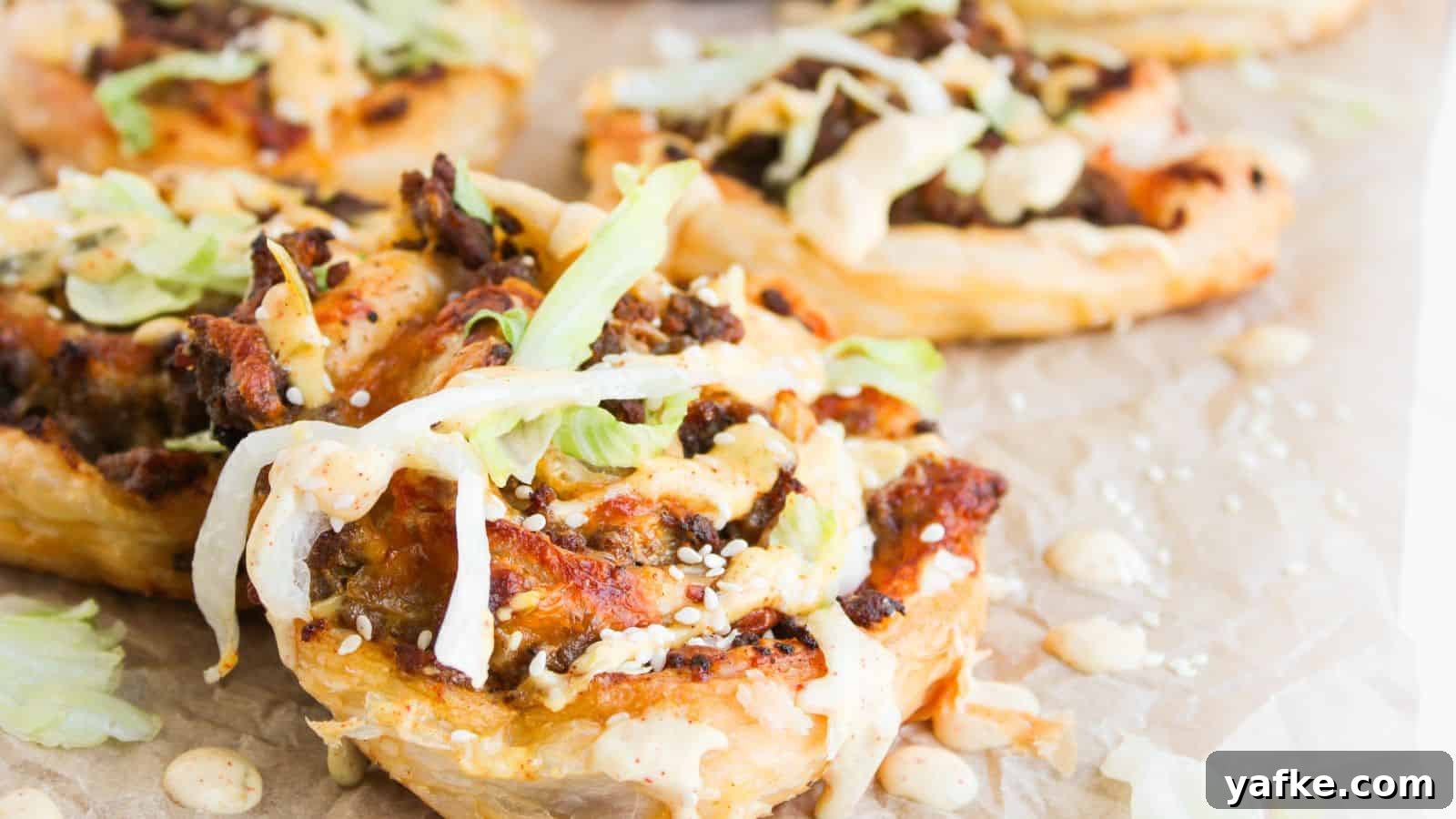 21 Fall Snacks I Tried: 9 Keepers 4 Close-up of puff pastry rounds topped with ground meat, shredded lettuce, sesame seeds, and a creamy sauce, arranged on parchment paper.