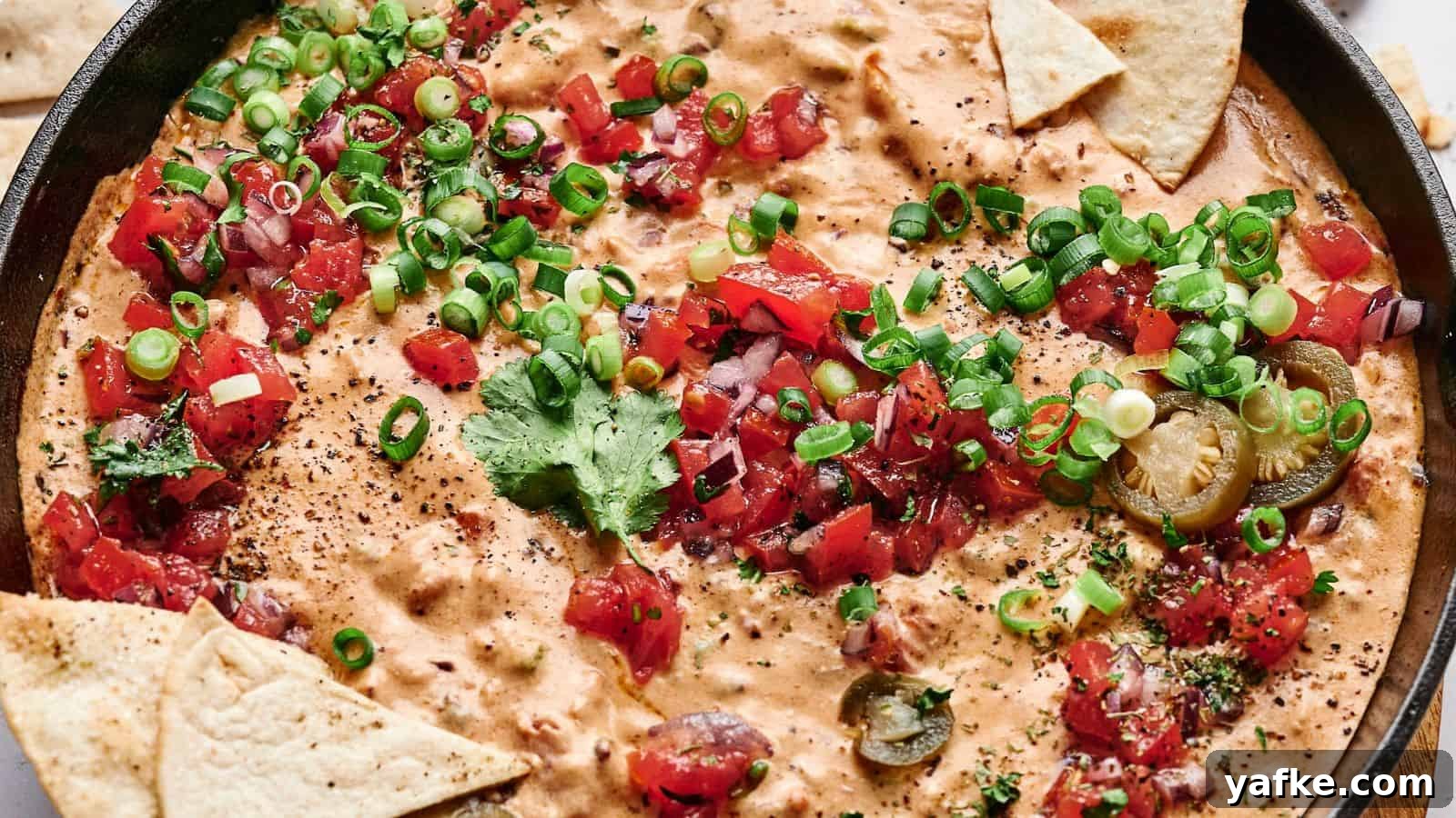 21 Fall Snacks I Tried: 9 Keepers 9 A skillet filled with creamy cheese dip topped with chopped tomatoes, green onions, cilantro, and sliced jalapeños, surrounded by triangular tortilla chips.