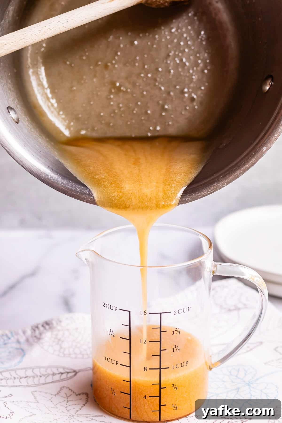 Homemade Buttermilk Syrup for Pancakes and Waffles 12 pouring syrup from a pot into a glass measuring cup on a white counter.