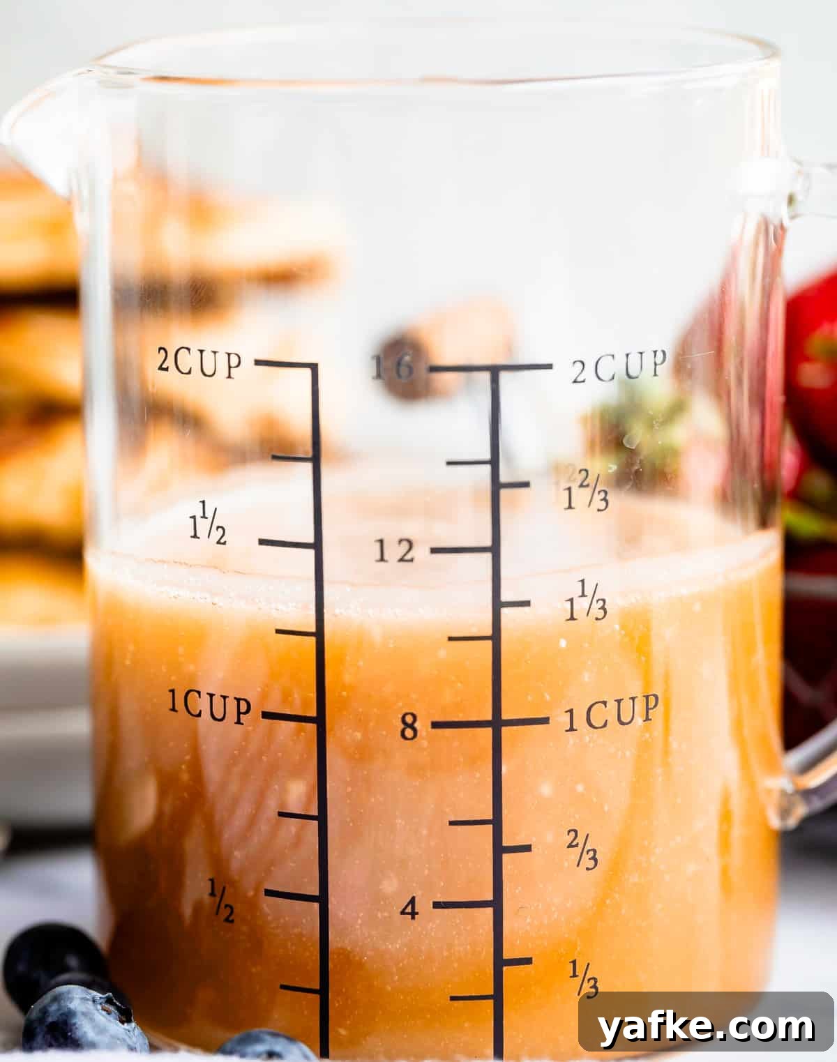 Homemade Buttermilk Syrup for Pancakes and Waffles 2 Buttermilk syrup in a glass measuring cup with blueberries in the foreground.