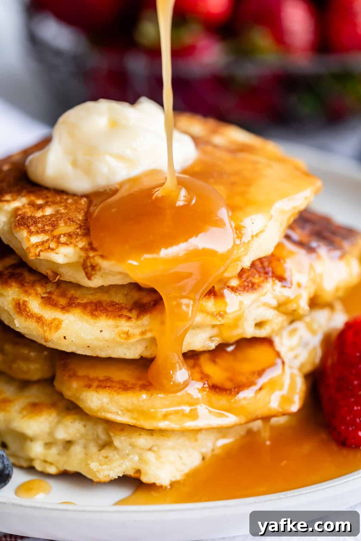 Homemade Buttermilk Syrup for Pancakes and Waffles 4 pouring buttermilk syrup over a stack of pancakes with butter and strawberry.
