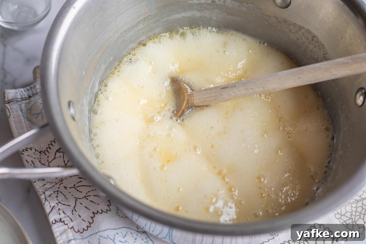 Homemade Buttermilk Syrup for Pancakes and Waffles 8 a metal pot of yellow boiling liquid with a wooden spoon.