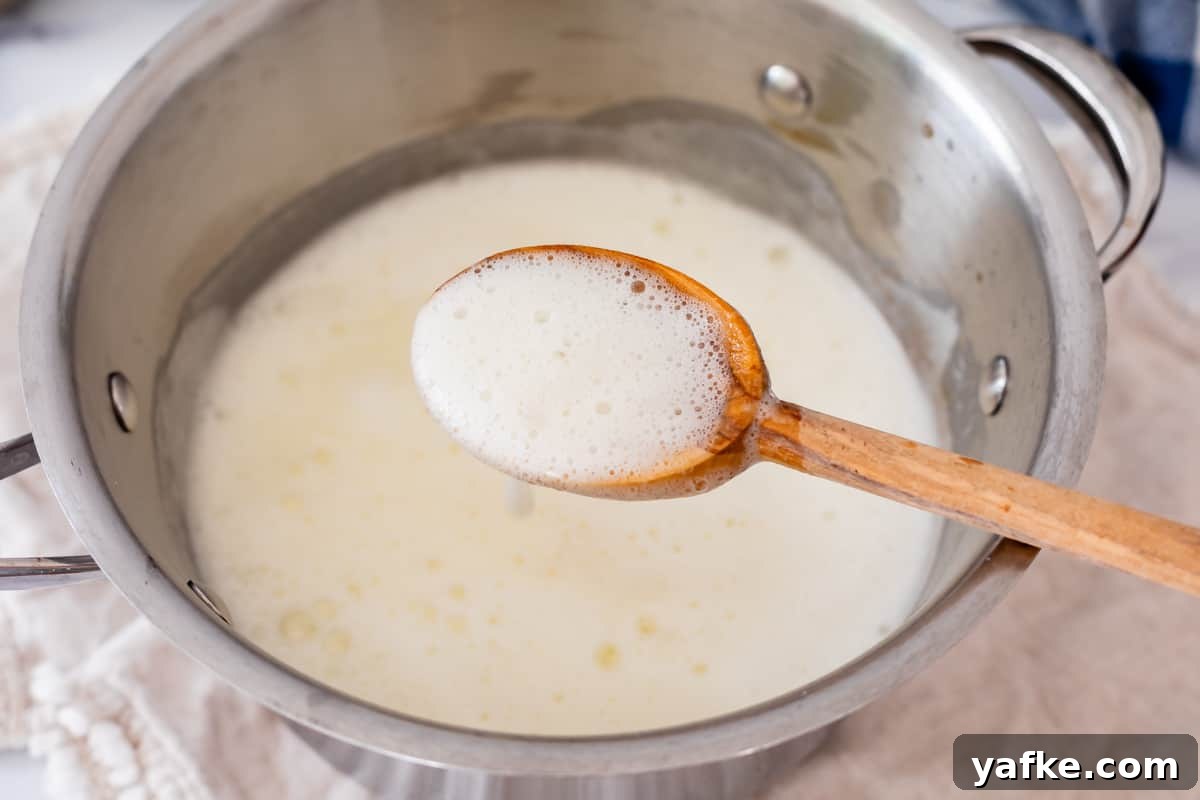 Homemade Buttermilk Syrup for Pancakes and Waffles 9 wooden spoon holding up bubbly white syrup from a metal spoon.