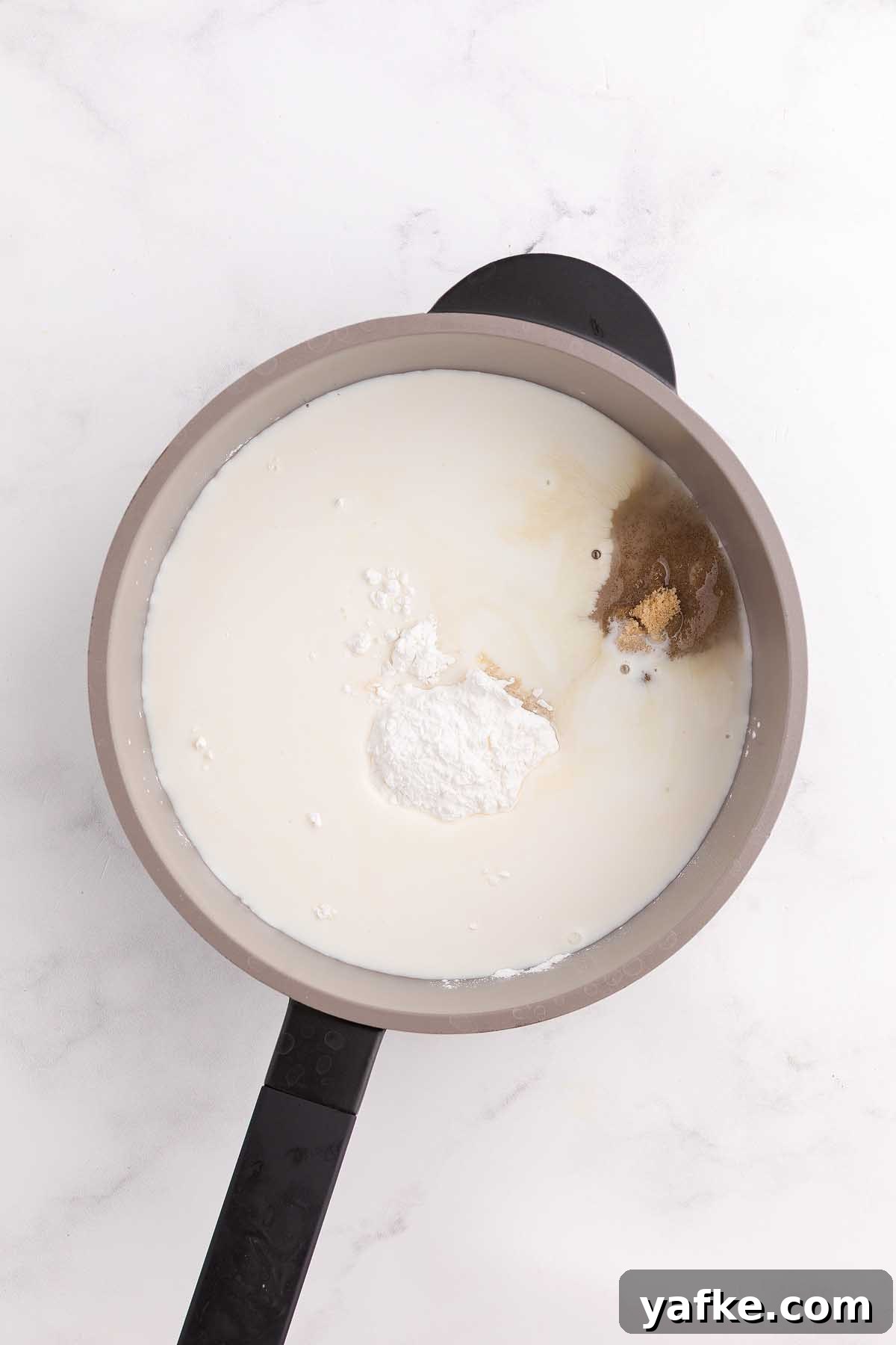 Coconut Meringue Pie with Toasted Coconut Topping 14 A saucepan with milk, brown sugar, cornstarch, and spices on a white marble surface—perfect for starting a classic coconut meringue pie.