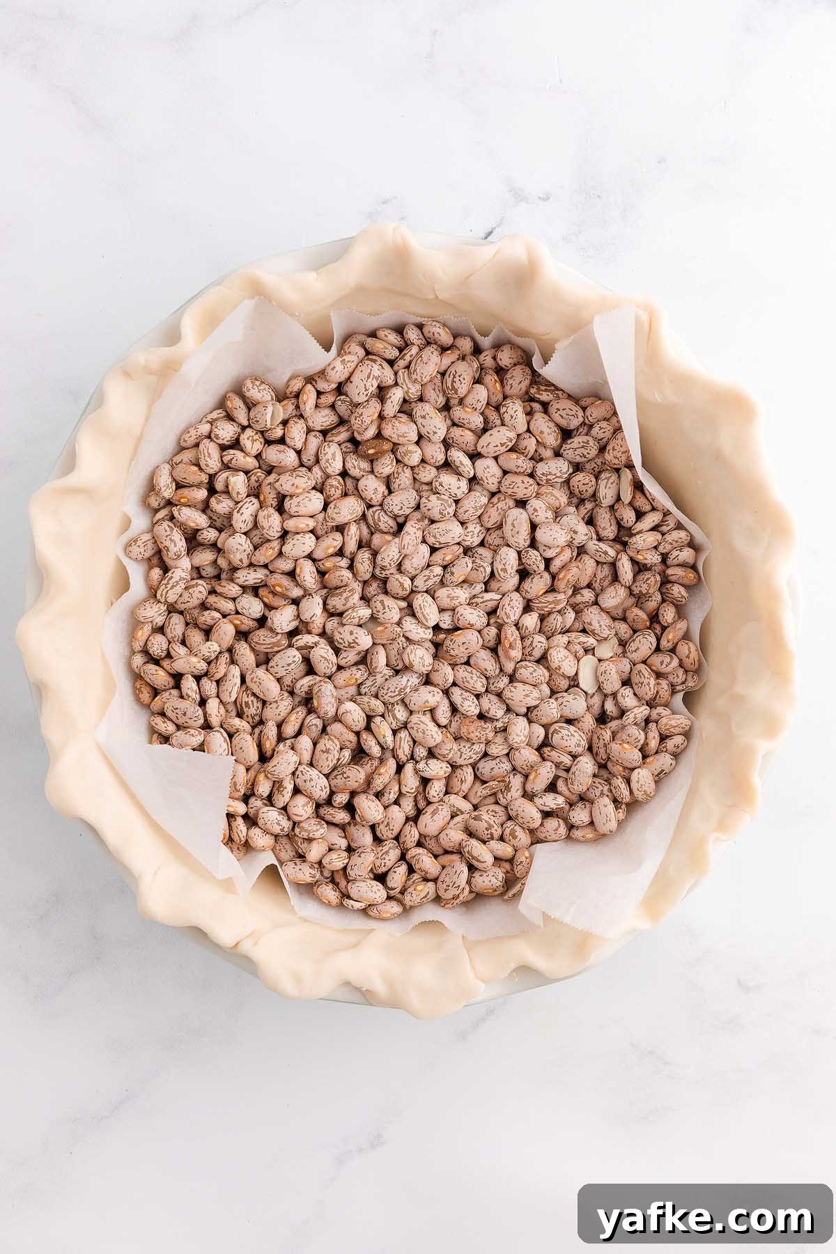 Coconut Meringue Pie with Toasted Coconut Topping 15 Unbaked pie crust in a pie dish filled with dried beans on parchment paper for blind baking, perfect as a base for a classic coconut meringue pie.