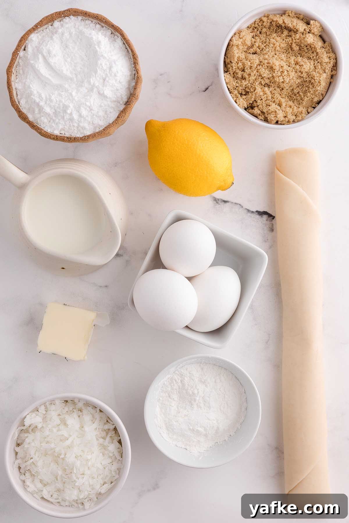 Coconut Meringue Pie with Toasted Coconut Topping 6 Baking ingredients for coconut meringue pie, including eggs, lemon, milk, butter, sugar, coconut, flour, and rolled dough on a marble surface.