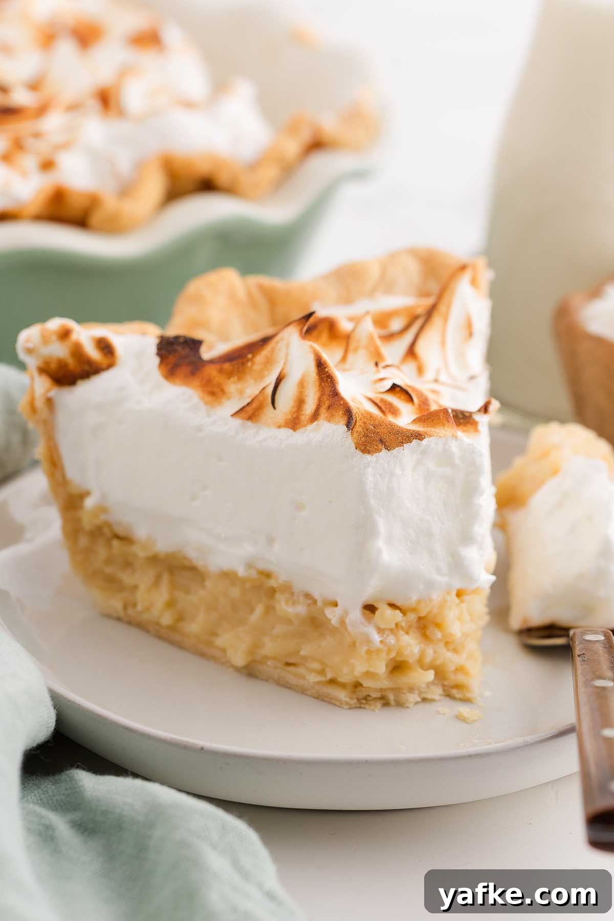 Coconut Meringue Pie with Toasted Coconut Topping 8 A slice of coconut meringue pie with toasted meringue topping sits on a white plate.