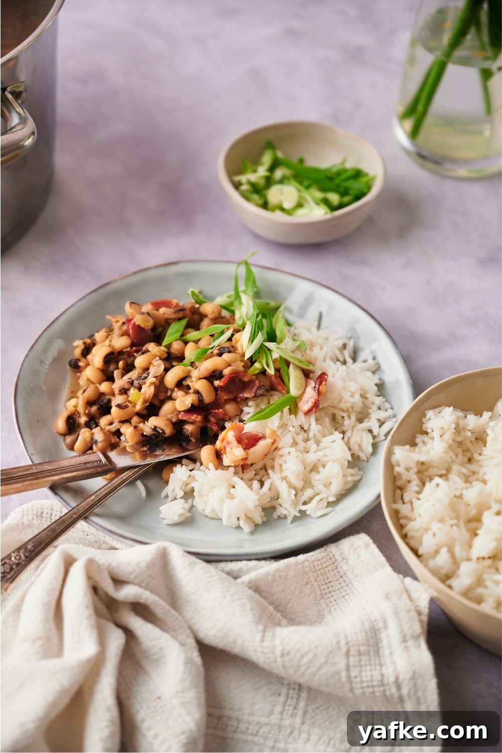 Blue bowl with hoppin' john, white rice, and a fork and knife next to a serving bowl of white rice.