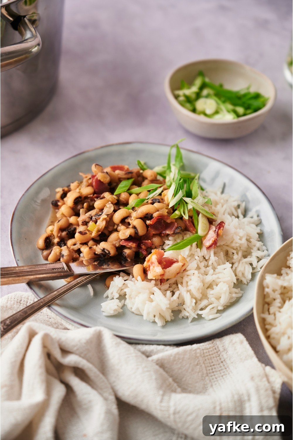 Blue bowl with hoppin' john, white rice, and a fork and knife.