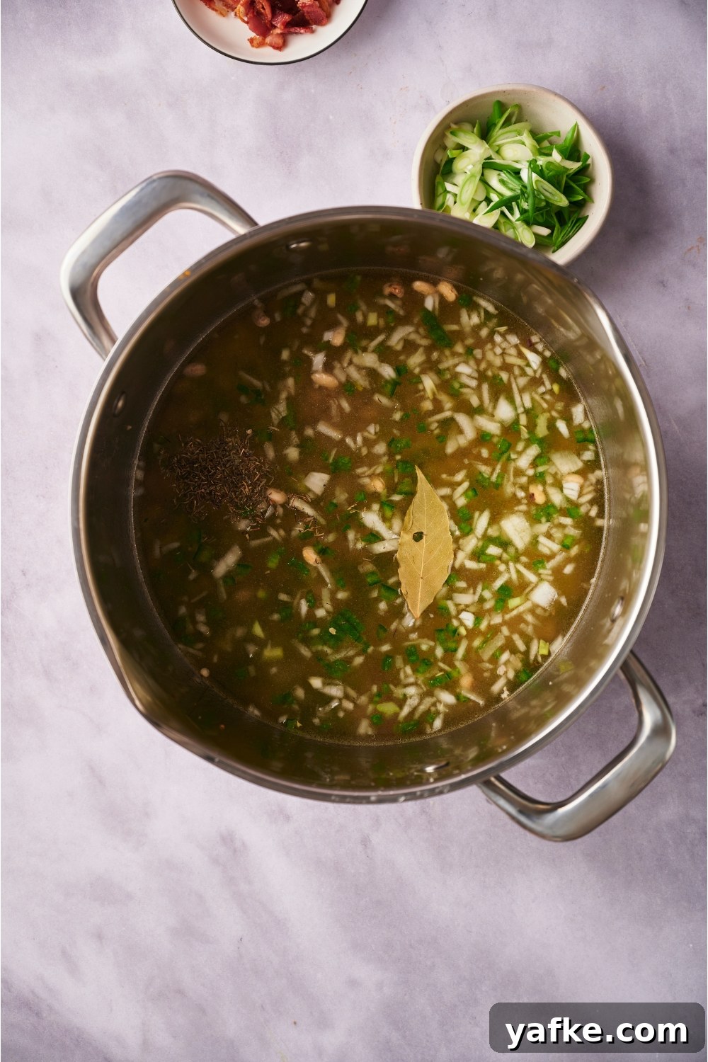 Large pot with diced onion, peppers, and a bay leaf in broth.