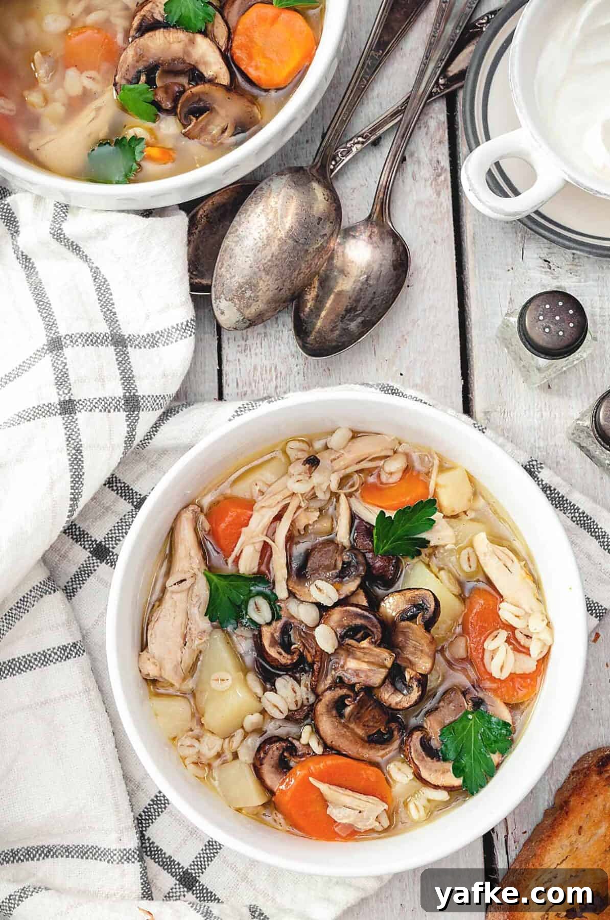 Polish Krupnik: Chicken, Barley and Mushroom Soup 6 Two bowls of chicken barley soup on a white wooden table with towel and spoons.
