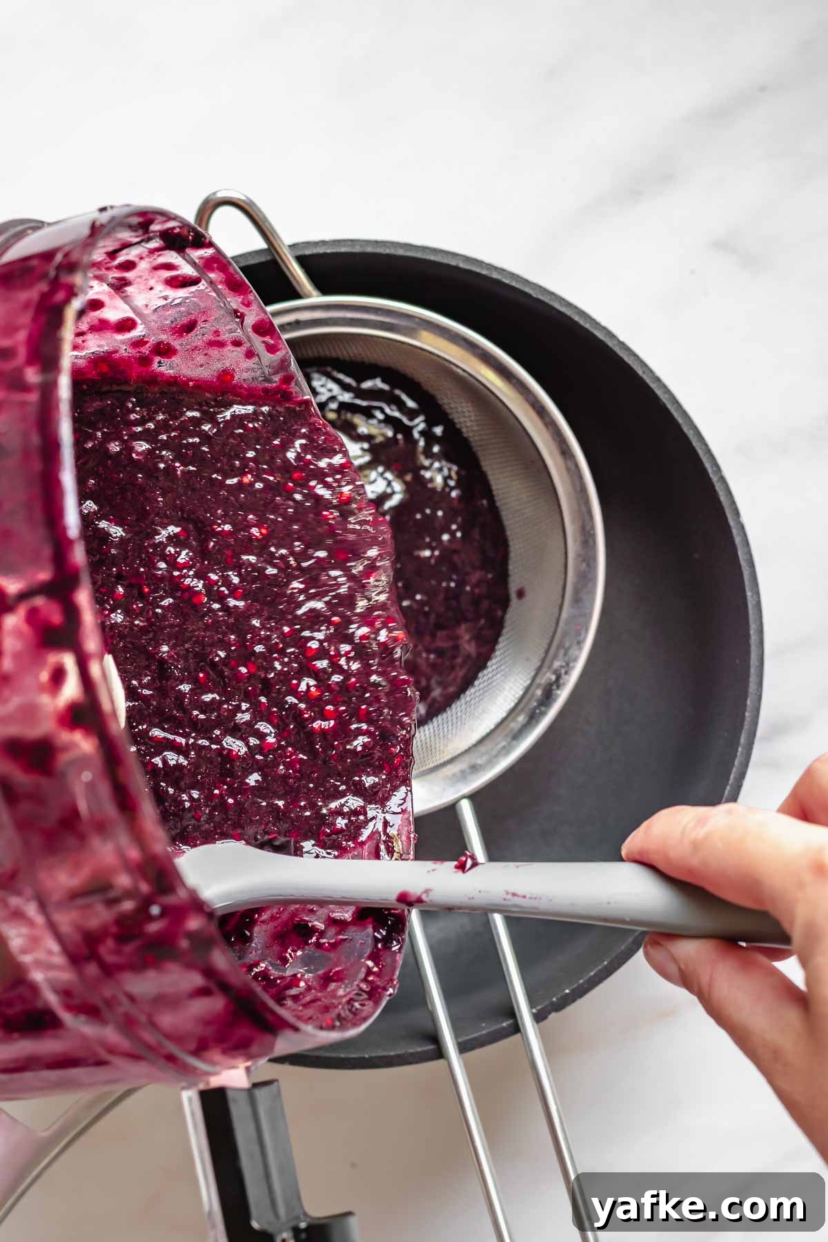 Creamy No-Churn Blackberry Chocolate Chip Ice Cream Recipe 5 Black raspberry puree pouring into a fine mesh strainer.