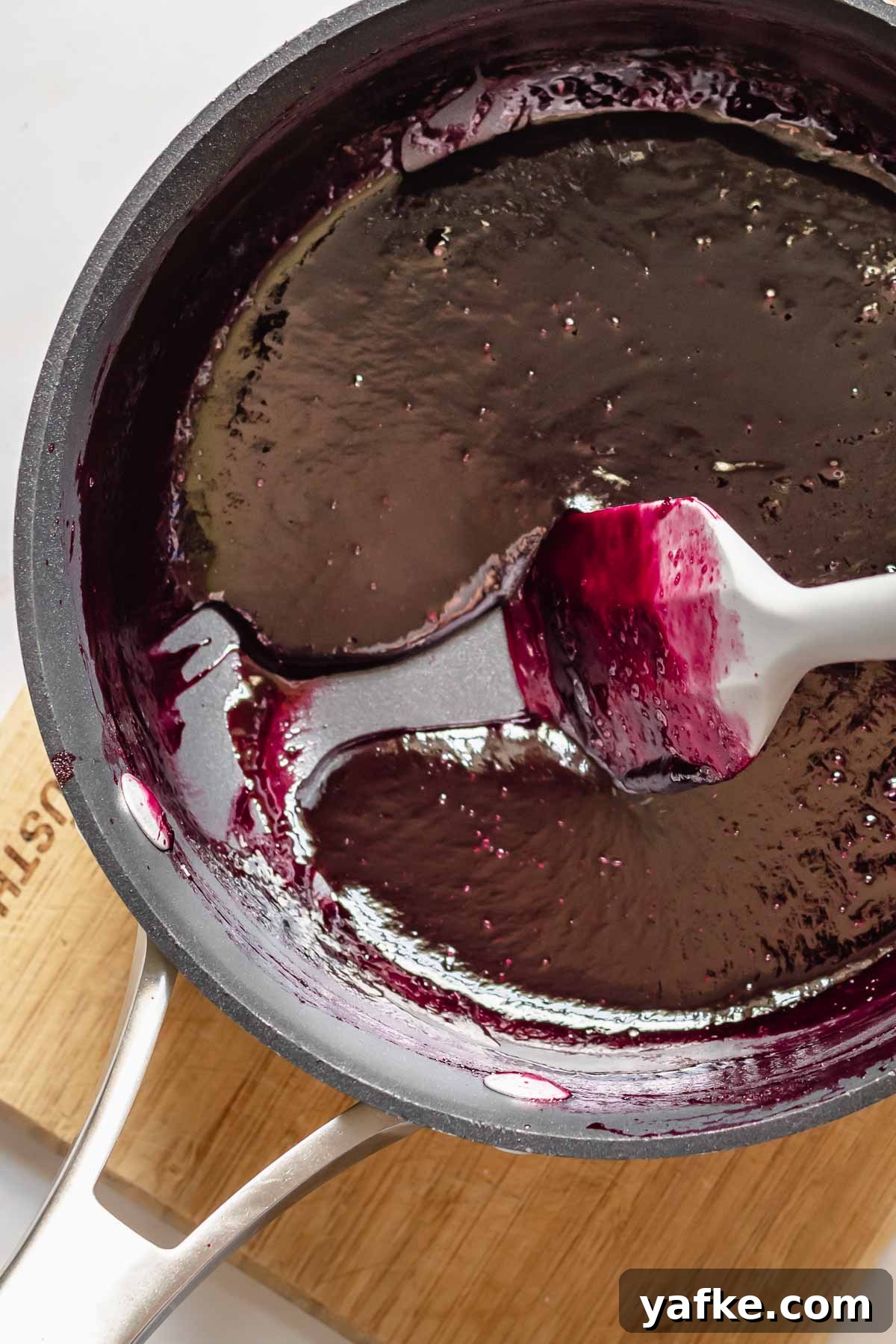 Creamy No-Churn Blackberry Chocolate Chip Ice Cream Recipe 6 A spatula drags reduced blackberry puree in a pot.