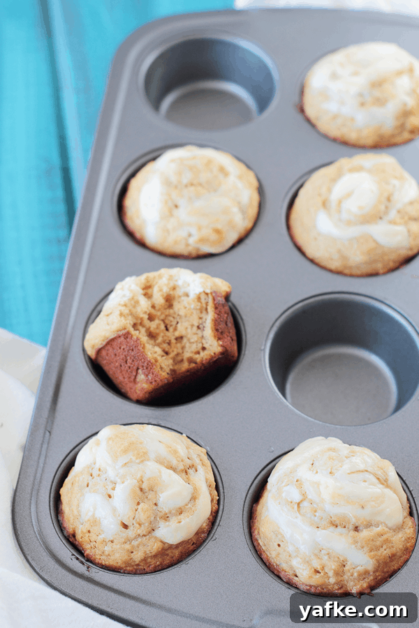 Banana Muffins with Cream Cheese Swirl Recipe 3 a muffin tin with banana muffins in them, some spots are empty and one muffin has a bite taken out of it