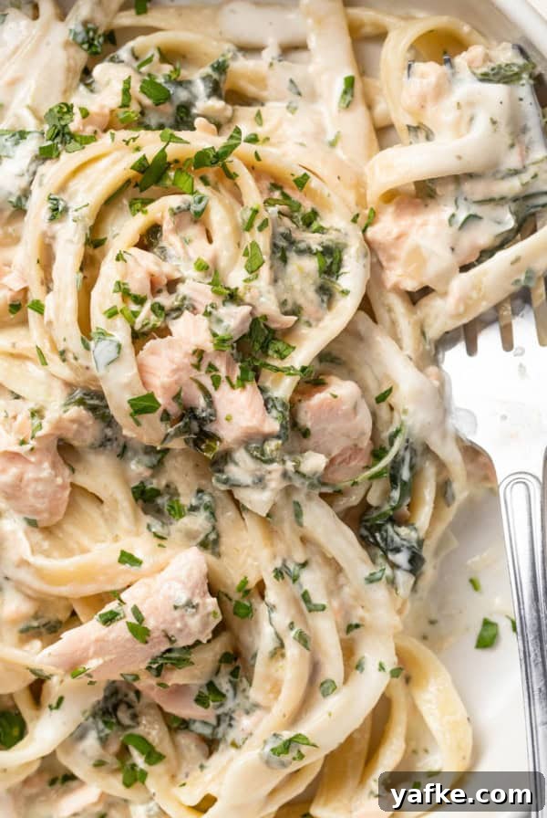 A fork scooping a creamy pasta with salmon and parsley.