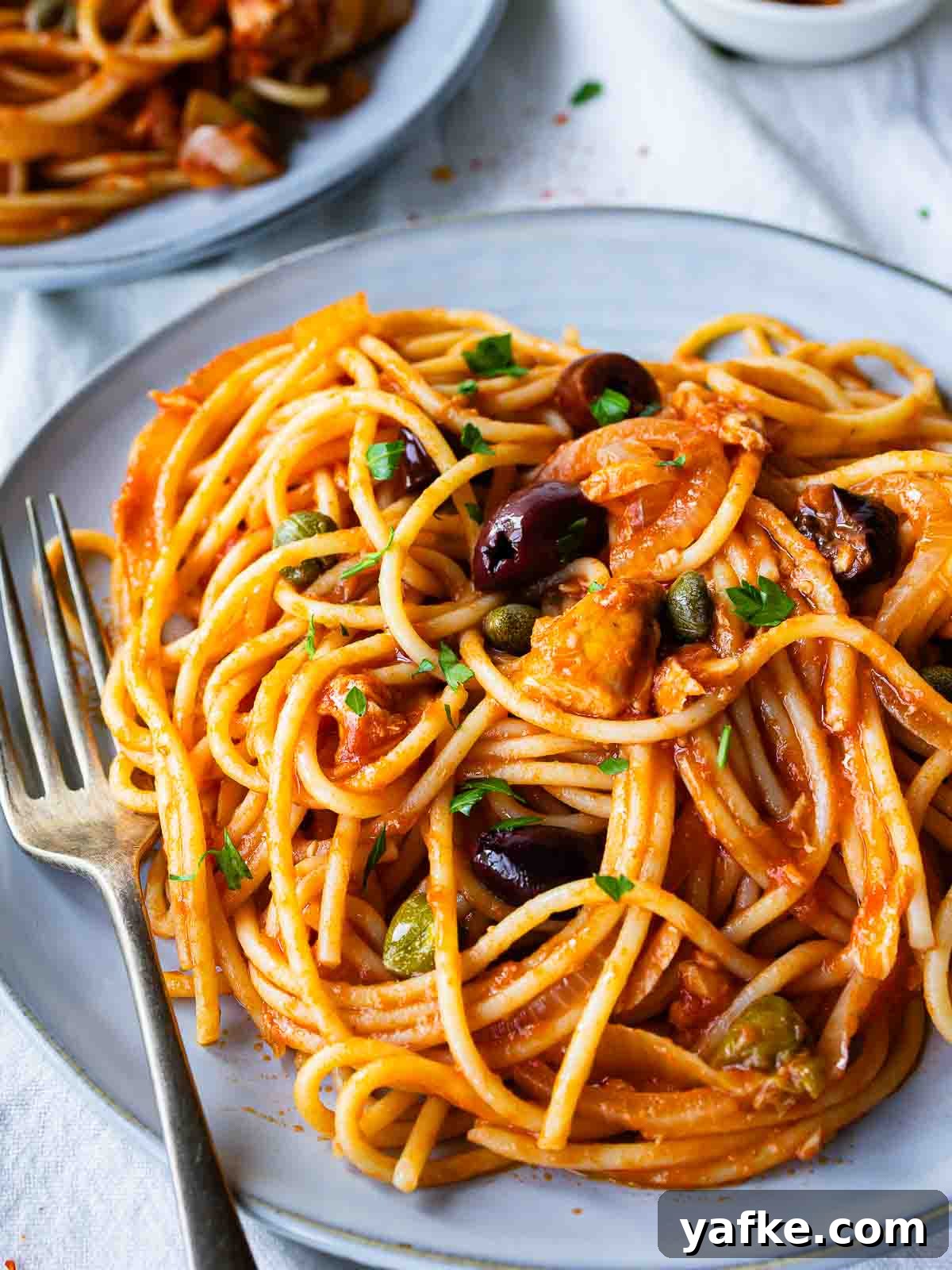 Creamy Tuna Pasta Recipe with Lemon & Capers 2 Plate of the tuna pasta recipe consisting of spaghetti in tomato sauce, with olives and chopped parsley.