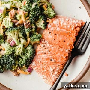 A piece of baked salmon on a plate with broccoli salad.