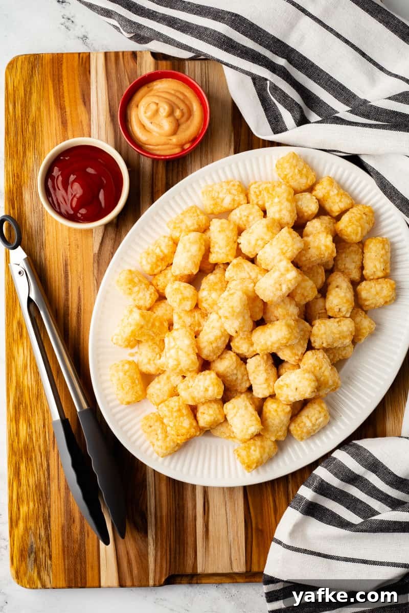 Crispy Air Fryer Tater Tots from Frozen 3 Frozen tater tots on a white plate, surrounded by condiments in small dishes.