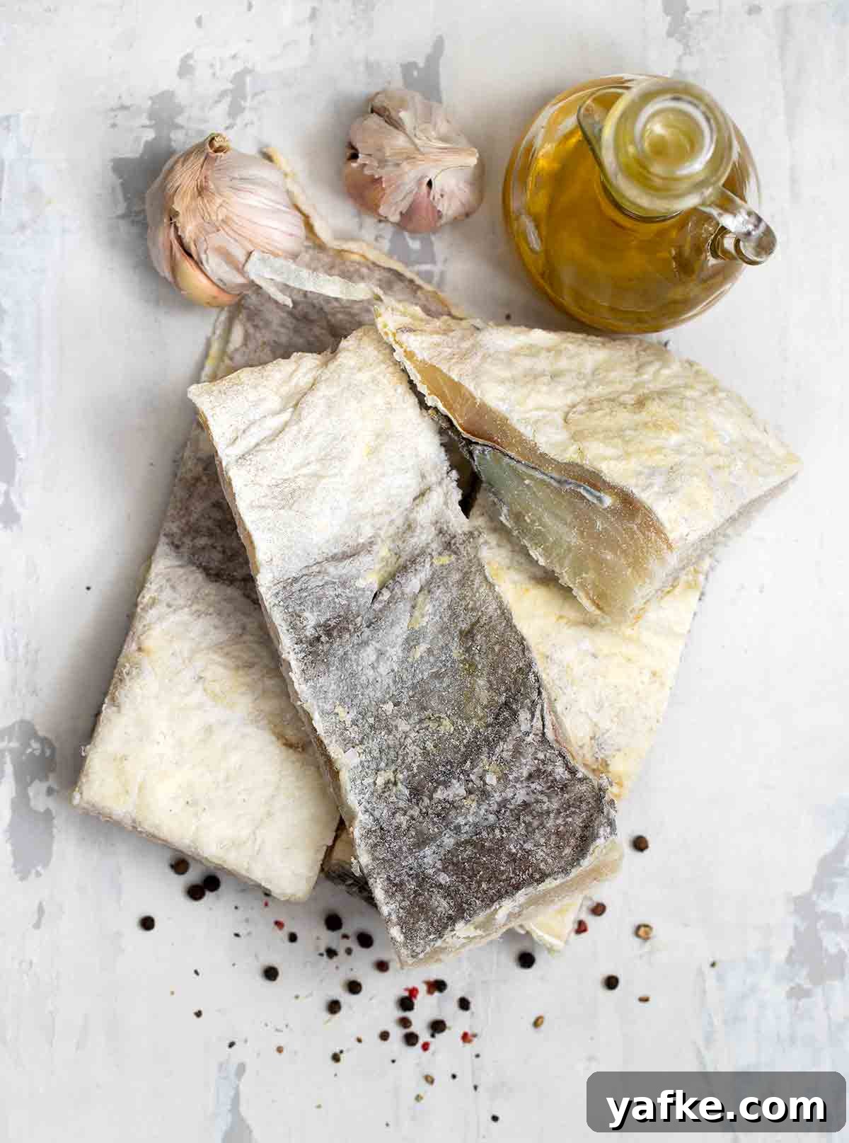 How to Buy, Soak and Cook Salt Cod (Bacalao) 3 Salt cod fillets, garlic, and olive oil on marble.