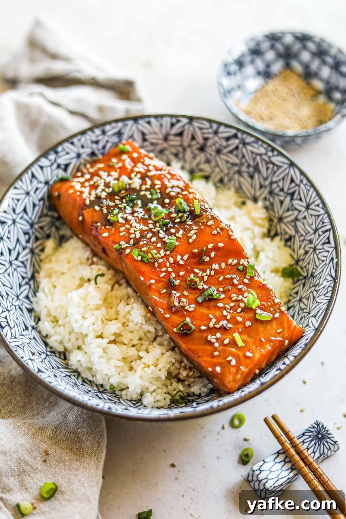 Teriyaki Salmon Donburi: Classic Japanese Rice Bowl 2 Teriyaki salmon rice bowl (donburi) in a blue Japanese porcelain bowl with chopsticks, garnished with sesame seeds and green onions.