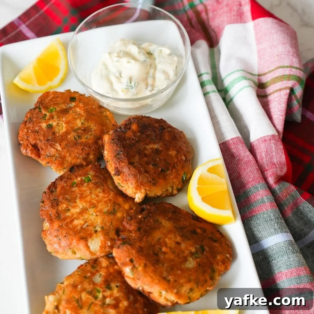 Crispy Salmon Croquettes Recipe with Lemon Dill Sauce 2 Golden brown salmon croquettes on a plate with a side of creamy tartar sauce.