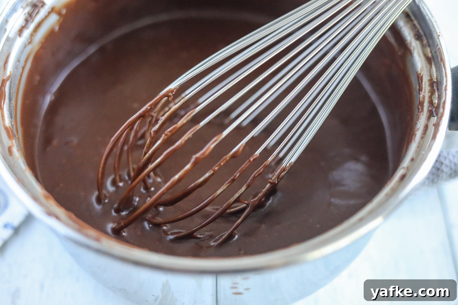 Decadent Chocolate Mound Cake Recipe 5 chocolate ganache in a small sauce pan with a whisk.