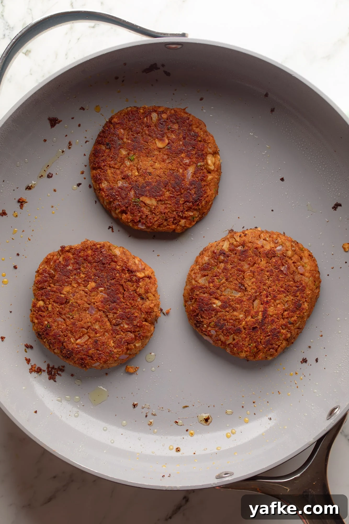Vegan Lentil Burgers with Garlic and Herbs 7 overhead view of 3 lentil burgers frying in a skillet.