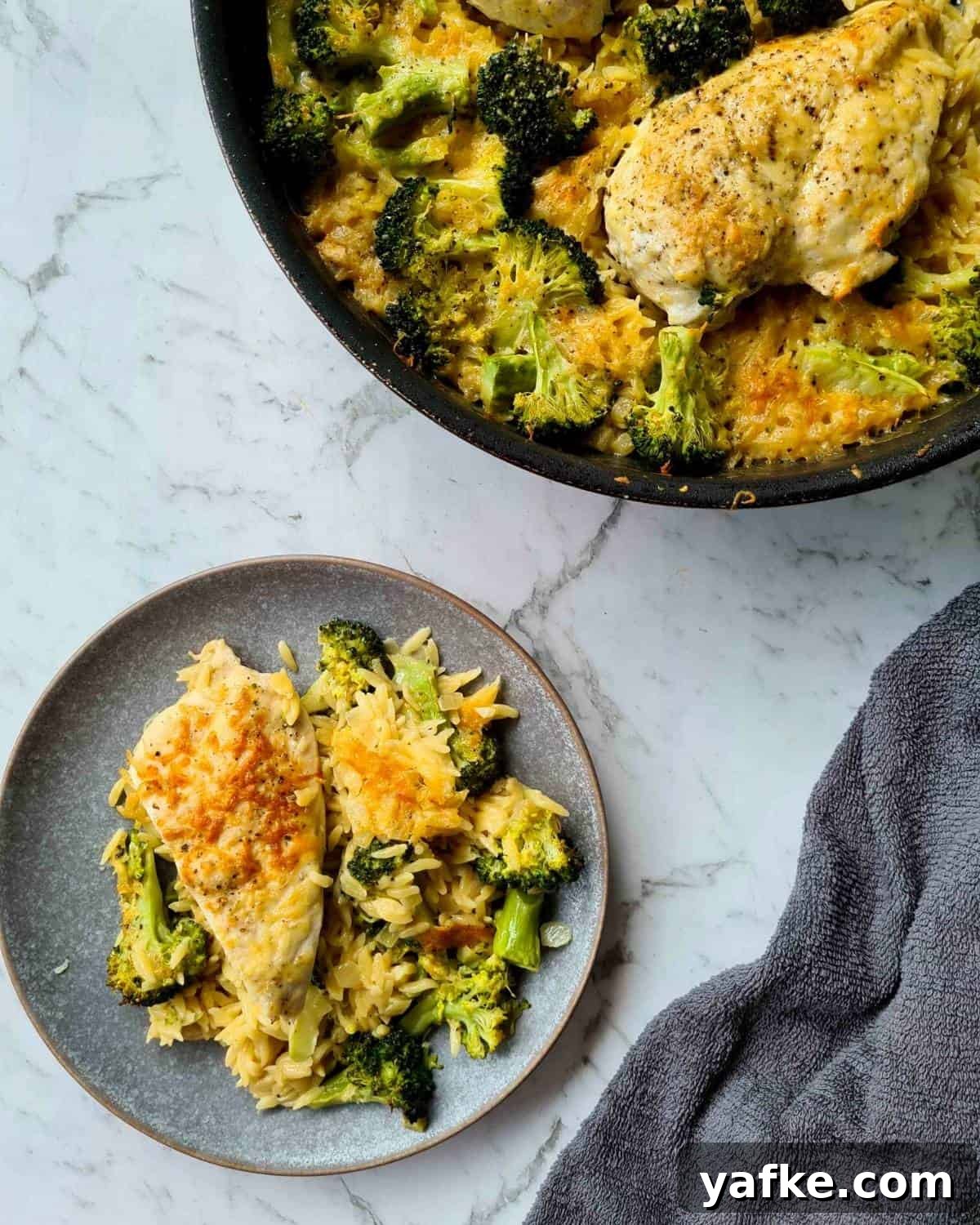 A plate serving of baked chicken and broccoli risoni with the full pan on the top right hand corner