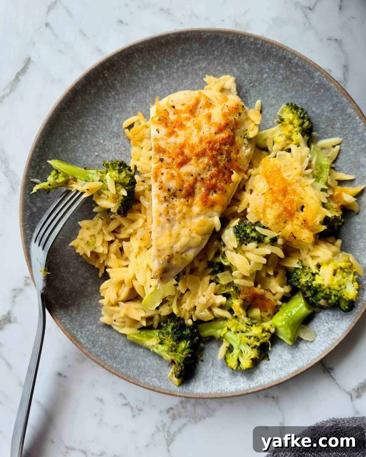 Close up of a plate of baked chicken and broccoli risoni