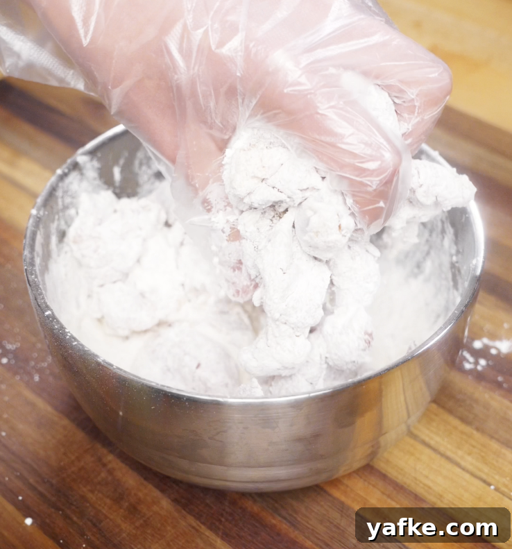 Crispy Sesame Chicken Recipe 4 Chicken pieces being tossed in a cornstarch and flour mixture until fully coated for frying.