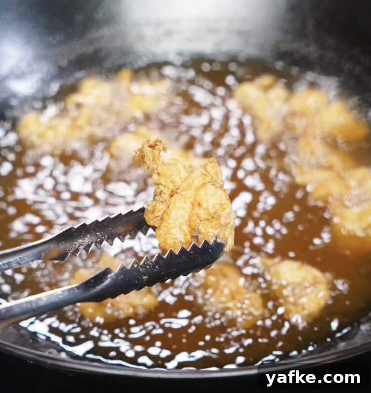 Crispy Sesame Chicken Recipe 6 Golden, crispy chicken thigh pieces being removed from the oil after the second fry.