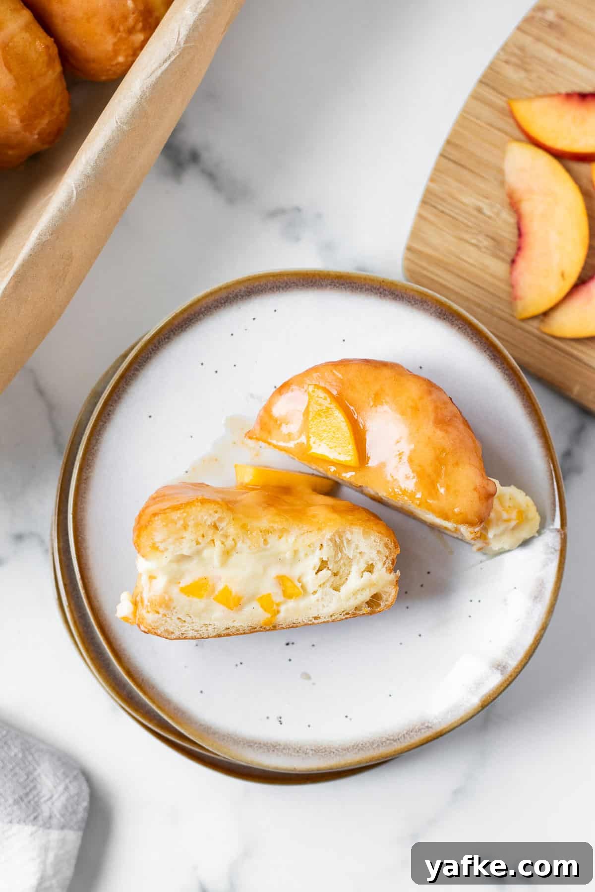 Peach Donuts with Peaches and Cream Filling 8 peach donut filled with cream split in half on a stack of plates with cutting board with peaches next to it