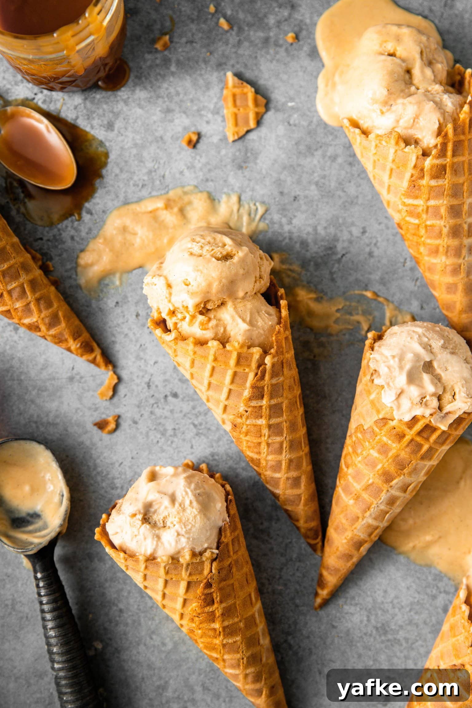 How to Make No Churn Bourbon Salted Caramel Ice Cream 2 Ice cream cones with scoops of bourbon salted caramel ice cream melting slightly showing creamy texture.
