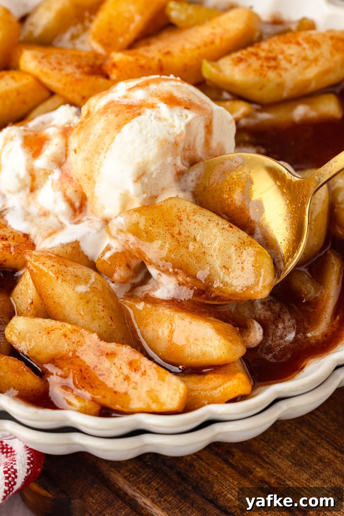 Skillet Fried Apples with Cinnamon and Brown Sugar 2 Fried apples with melting vanilla ice cream and cinnamon in a white dish with gold spoon.