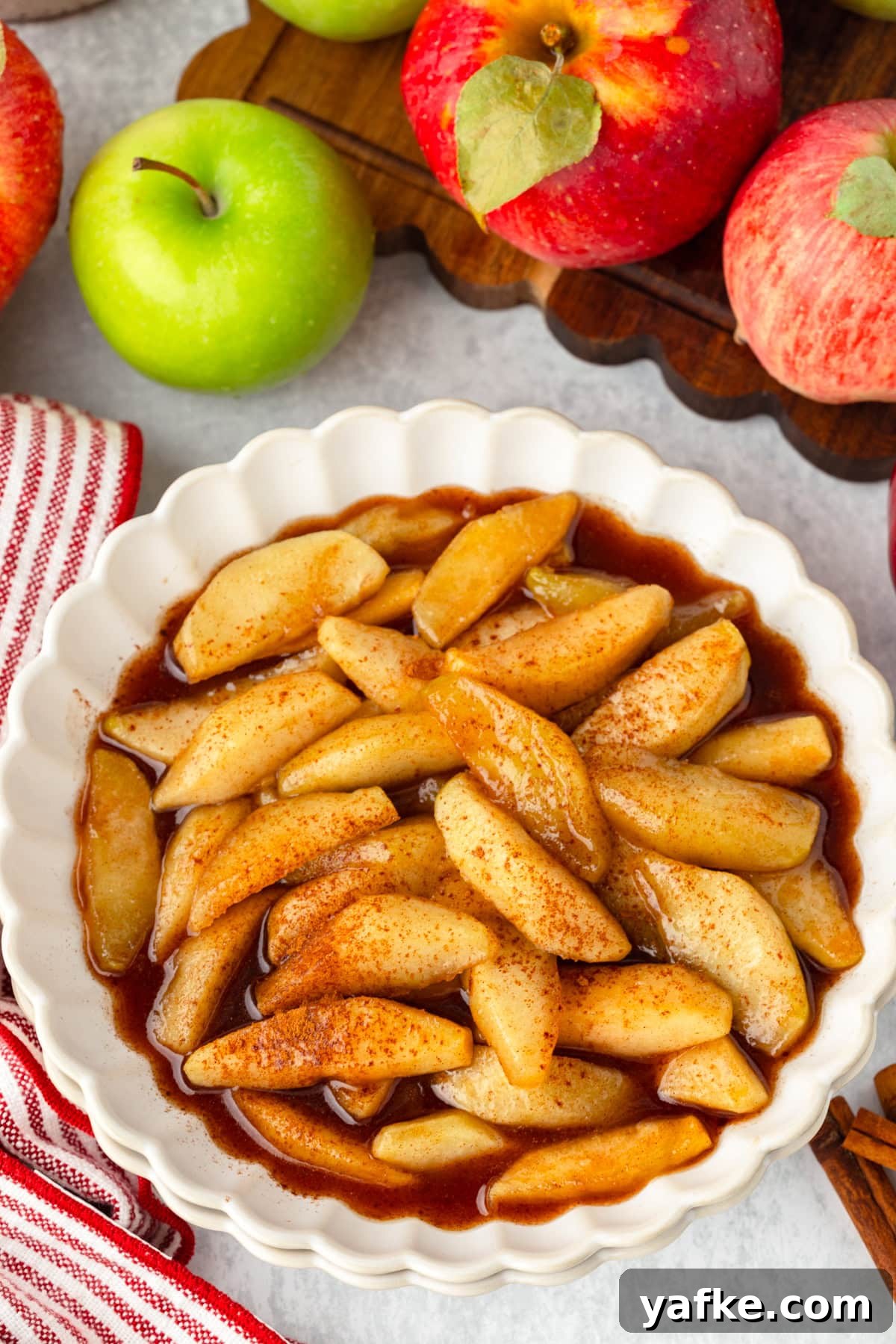 Skillet Fried Apples with Cinnamon and Brown Sugar 7 Fried apples in a white bowl surrounded by red and green apples.