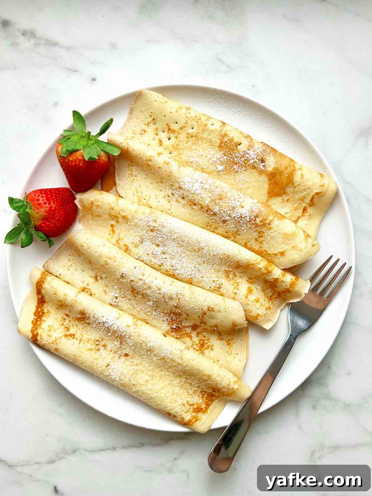 Authentic Swedish Pancake Recipe: Thin Crepe-Style Pancakes 2 plate of Swedish pancakes rolled with powdered sugar sprinkled on top.