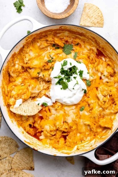 Creamy White Queso Dip Recipe for Tacos and Chips 8 White skillet filled with cheesy chicken enchilada dip, topped with sour cream and with a tortilla chip stuck in it.