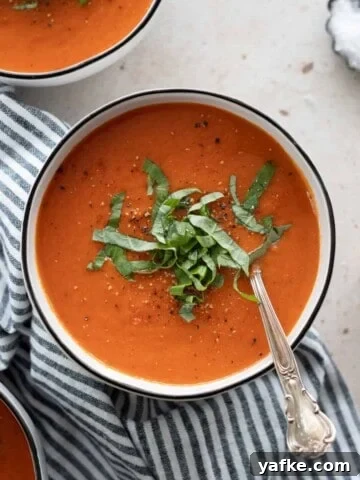 Roasted red pepper and tomato soup on a bowl with a spoon.