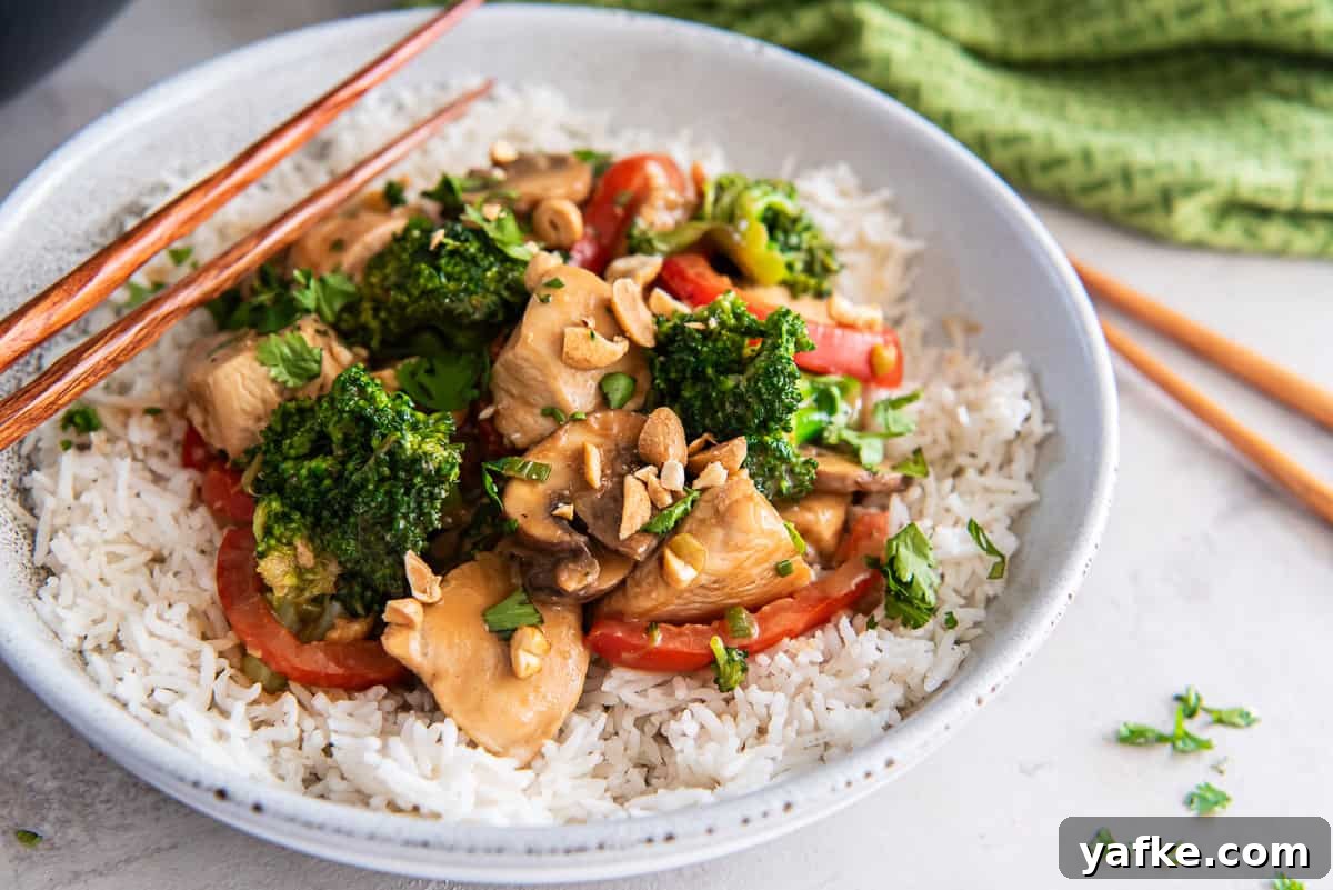 Peanut Chicken Stir-Fry Recipe with Vegetables 4 Chopsticks resting on a bowl of rice topped with peanut chicken stir fry.