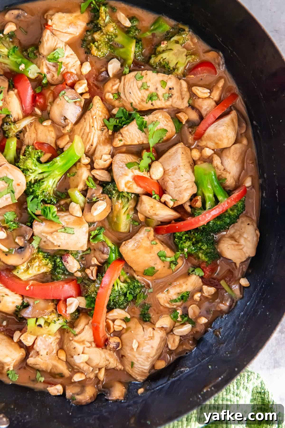 Peanut Chicken Stir-Fry Recipe with Vegetables 6 A dark skillet filled with a chicken a veggie stir fry with peanut sauce.
