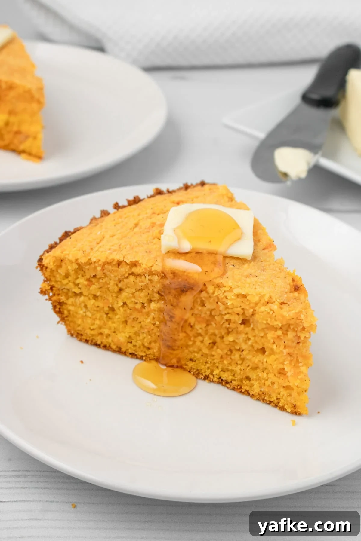 Southern Sweet Potato Cornbread with Maple and Pecans 2 An image of a slice of sweet potato cornbread on a plate with butter and honey on top.
